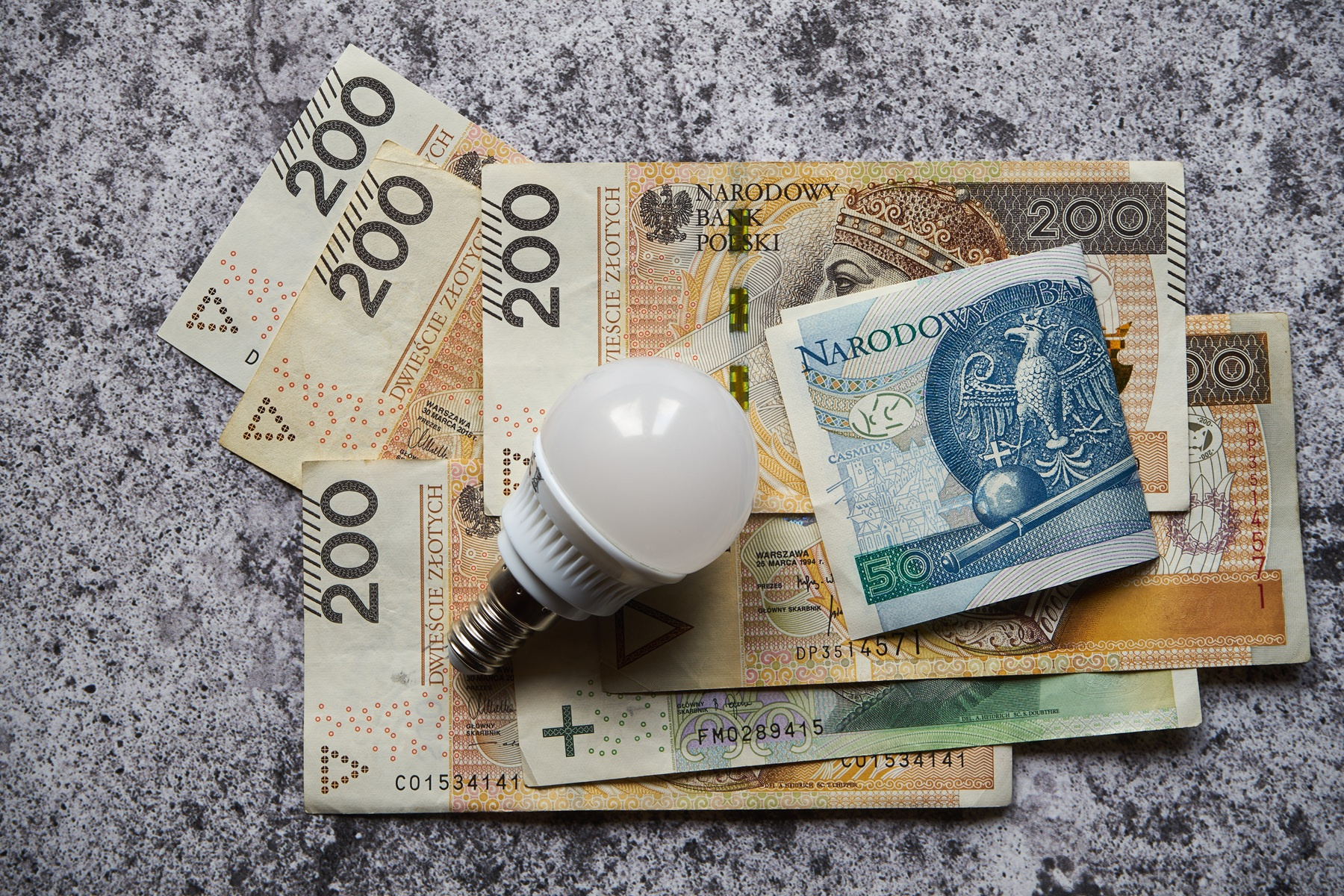 Żarówka LED obok banknotów złotówkowych symbolizujących oszczędności na rachunkach za prąd w systemie net billing